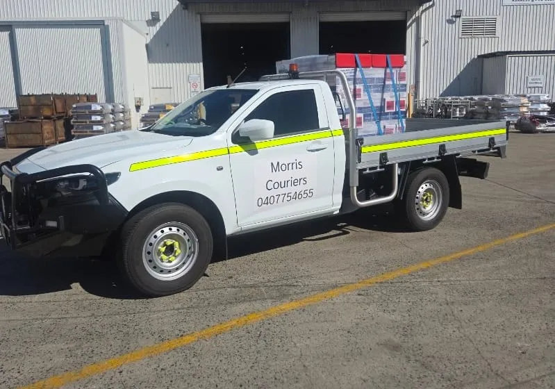 A Morris Couriers ute loaded with strapped freight outside a supplier's warehouse.