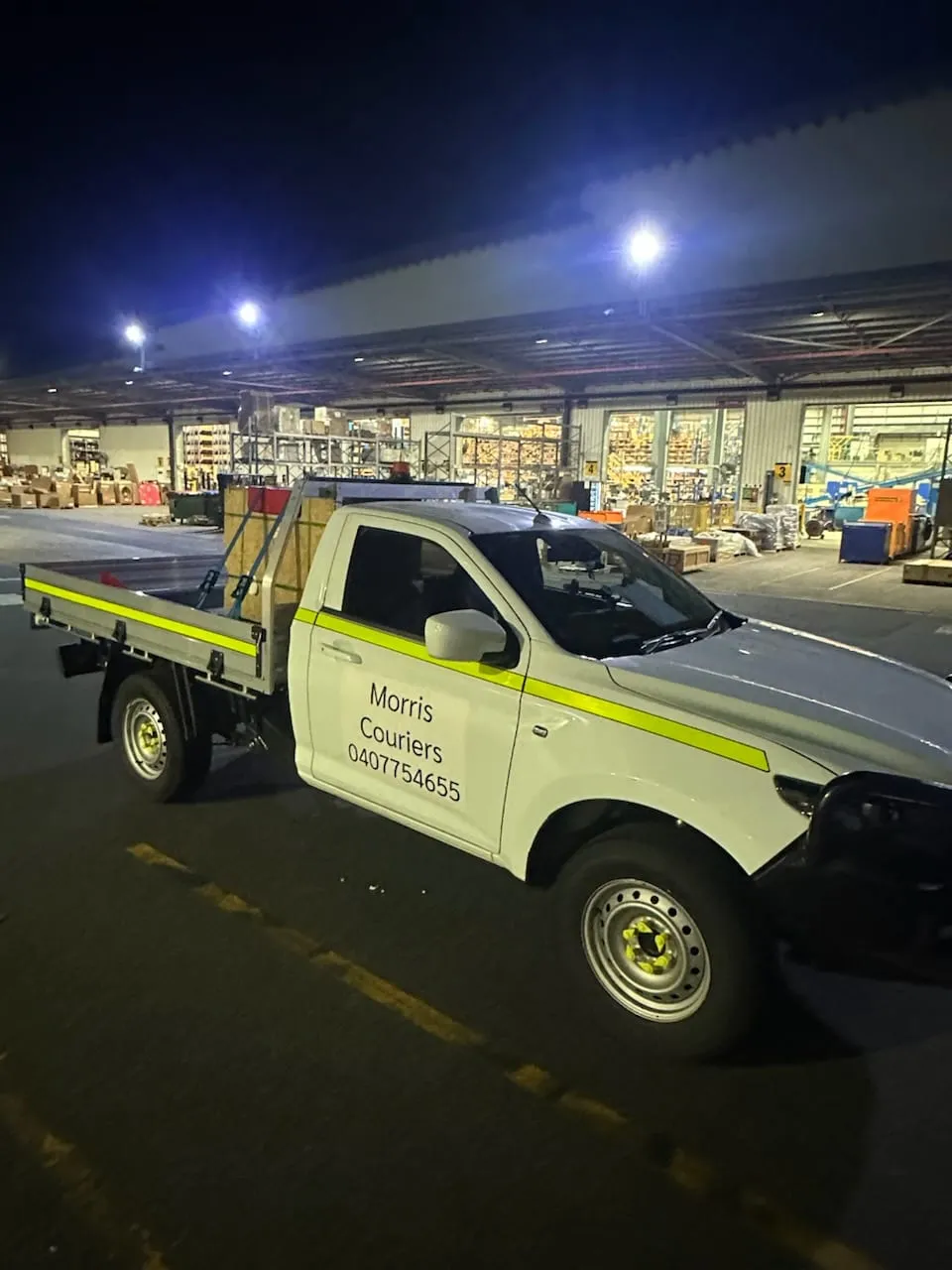 A Morris Couriers ute loaded and ready to leave a warehouse after dark.